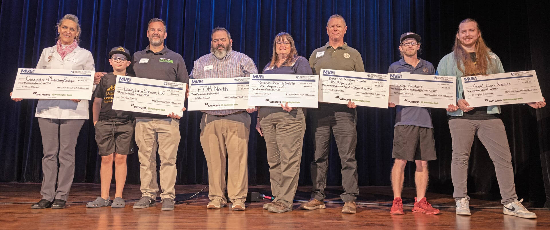 eight people standing on stage holding oversized checks